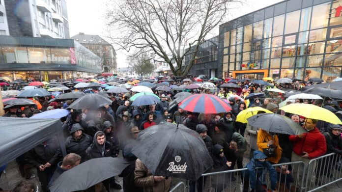 Eine große Menge an Menschen kommt auf einem Platz in Karlsruhe bei Regen zusammen, um zu demonstrieren