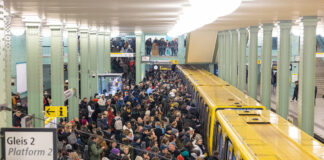 An einem Bahnsteig befinden sich viele Menschen, die gerade in einen Zug oder eine S-Bahn einsteigen wollen. Es herrscht dichtes Gedrängel, denn die Haltestelle ist komplett überfüllt.