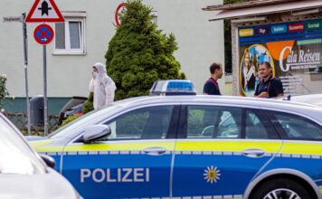 Ein Einsatzfahrzeug der Polizei und im Hintergrund Mitarbeiter der Polizei. Die Spurensicherung ist am Tatort angekommen und sichert die Spuren vor Ort, um den Täter zu finden.