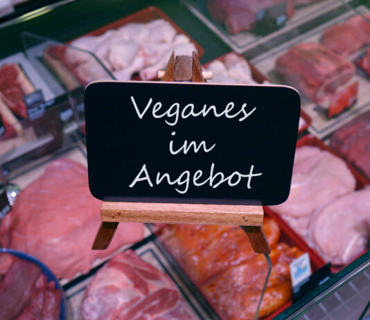 Eine Fleischtheke in einer Metzgerei mit einem Schild, das Veganes anbietet.