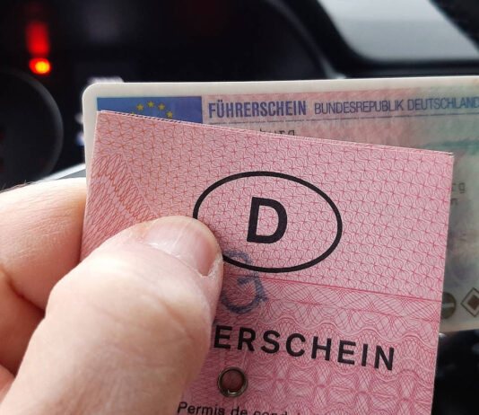 Jemand sitzt im Auto und hält vorm Armaturenbrett einen rosa Führerschein in Papierform in der Hand. Dahinter hält er die Plastikkarte der neueren Version. Beides sind deutsche Führerscheine.