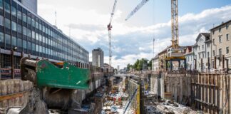 Eine Großbaustelle mitten in der Innenstadt von Karlsruhe, mit Baufahrzeugen und einem Kran. Die Fahrzeuge stehen im Sand zwischen Büro- und Wohnhäusern.