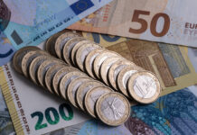 Geld liegt auf dem Tisch. Unzählige 1-Euro-Münzen liegen in einer Reihe auf verschiedenen Geldscheinen. Darunter befinden sich ein gelber 200-Euro-Schein, sowie ein Fünfziger und Zwanziger. Das Bargeld symbolisiert einen neuen Zuschuss.