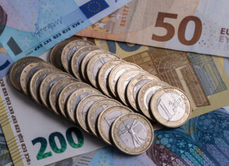 Geld liegt auf dem Tisch. Unzählige 1-Euro-Münzen liegen in einer Reihe auf verschiedenen Geldscheinen. Darunter befinden sich ein gelber 200-Euro-Schein, sowie ein Fünfziger und Zwanziger. Das Bargeld symbolisiert einen neuen Zuschuss.