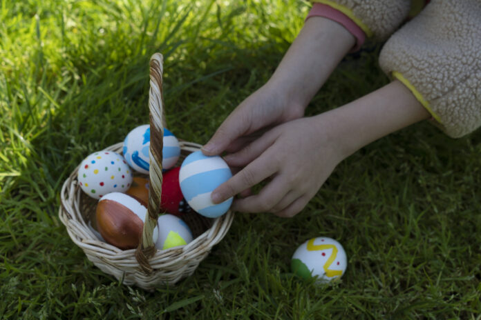Ein Mädchen nimmt aus einem Osterkorb mit Eiern ein buntes Ei heraus.