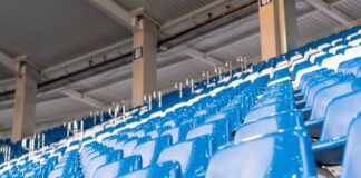 Leere blaue Sitze auf einer Tribüne in einem Stadion. Diese Sitzgelegenheiten befinden sich im Wildpark Stadion und zeigen direkt auf das Spielfeld.