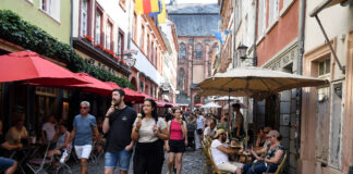 Mehrere Touristen bummeln durch eine enge, pittoreske Altstadt. Cafés, Touristenläden, Kioske und unzählige Straßenverkäufer säumen zusammen mit Touristen aus aller Welt die Kopfsteinpflaster-Straßen der Innenstadt.