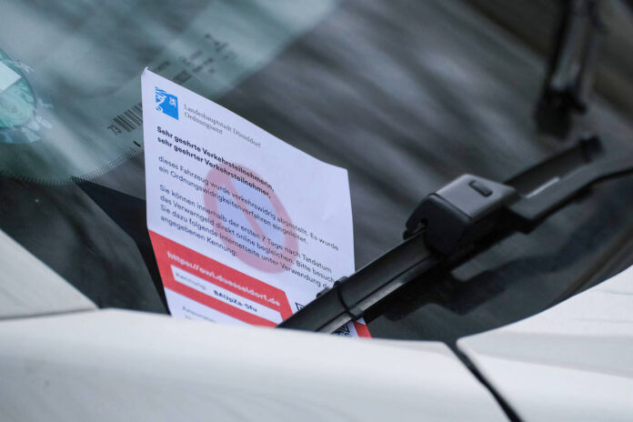 Ein Strafzettel, an eine Windschutzscheibe geklemmt, zeigt an, dass ein Auto falsch abgestellt wurde, was weitestgehend zu einem Fahrverbot führen kann.