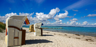 Strandkörbe an einem langen weißen Sandstrand. Im Hintergrund ist das Meer zu erkennen. Der Himmel ist blau und der Strand ist frei von Menschen.