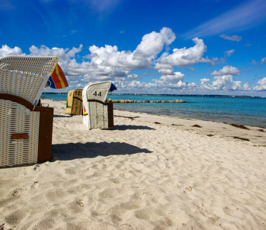 Strandkörbe an einem langen weißen Sandstrand. Im Hintergrund ist das Meer zu erkennen. Der Himmel ist blau und der Strand ist frei von Menschen.