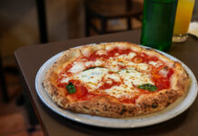 Eine frisch zubereitete Pizza Margherita wird serviert auf einem weißen Teller im Restaurant. Der Belag besteht Tomatensauce, Mozzarella, Basilikum und Olivenöl.