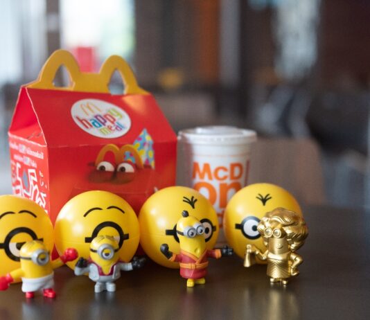 Ein Happy Meal und ein Getränk stehen auf dem Tisch. Davor stehen verschiedene Minion-Figuren.