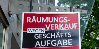 Ein schwarz-rotes, großes Schild in einer Einkaufsstraße in der Nahaufnahme hat in weißen Buchstaben den Text "Räumungsverkauf wegen Geschäftsaufgabe" in fetten Buchstaben gedruckt.