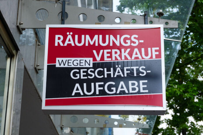 Ein schwarz-rotes, großes Schild in einer Einkaufsstraße in der Nahaufnahme hat in weißen Buchstaben den Text "Räumungsverkauf wegen Geschäftsaufgabe" in fetten Buchstaben gedruckt.