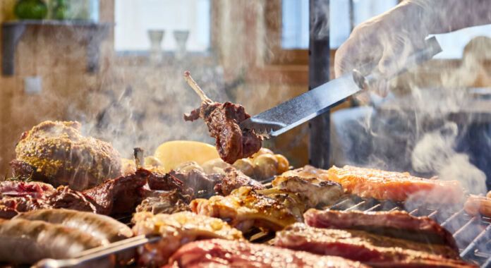 Das Fleisch wird auf den Grill gelegt, Rippchen, Würste, Hühnchen. Es handelt sich um ein Grillgericht. Verschiedene Portionen Fleisch werden gegart und den Gästen serviert.