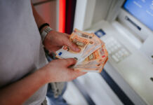 Junge Männerhände halten mehrere 50-Euro-Scheine fest. Der Mann steht offenbar vor einem Geldautomaten und zählt sein Geld, welches er gerade abgeholt hat, nach. An seinem linken Handgelenk befindet sich eine Uhr.