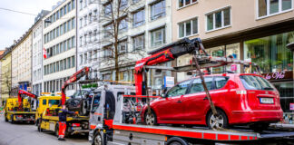 Ein rotes und ein blaues Auto werden von jeweils einem Abschleppwagen abgeschleppt. Entweder sie standen im Parkverbot oder es war eine Auto-Panne. Drei Abschleppwagen stehen in einer Reihe am Straßenrand. Im Hintergrund sind Häuserwände einer Altstadt.