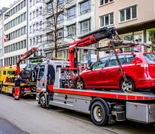 Ein rotes und ein blaues Auto werden von jeweils einem Abschleppwagen abgeschleppt. Entweder sie standen im Parkverbot oder es war eine Auto-Panne. Drei Abschleppwagen stehen in einer Reihe am Straßenrand. Im Hintergrund sind Häuserwände einer Altstadt.