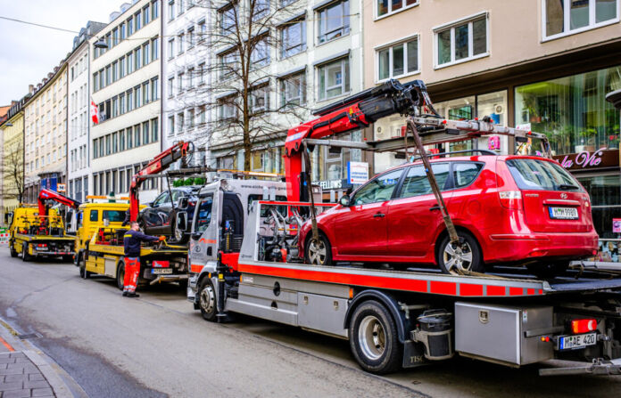 Ein rotes und ein blaues Auto werden von jeweils einem Abschleppwagen abgeschleppt. Entweder sie standen im Parkverbot oder es war eine Auto-Panne. Drei Abschleppwagen stehen in einer Reihe am Straßenrand. Im Hintergrund sind Häuserwände einer Altstadt.