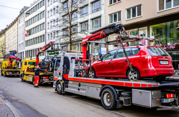 Ein rotes und ein blaues Auto werden von jeweils einem Abschleppwagen abgeschleppt. Entweder sie standen im Parkverbot oder es war eine Auto-Panne. Drei Abschleppwagen stehen in einer Reihe am Straßenrand. Im Hintergrund sind Häuserwände einer Altstadt.