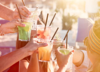 Mehrere Freunde halten Gläser mit einem Cocktail und Strohhalm in der Hand und stoßen bei gutem Wetter im Sommer an.