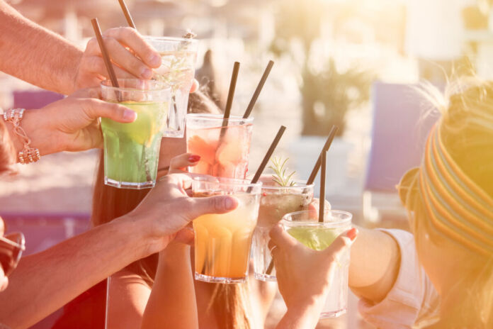Mehrere Freunde halten Gläser mit einem Cocktail und Strohhalm in der Hand und stoßen bei gutem Wetter im Sommer an.