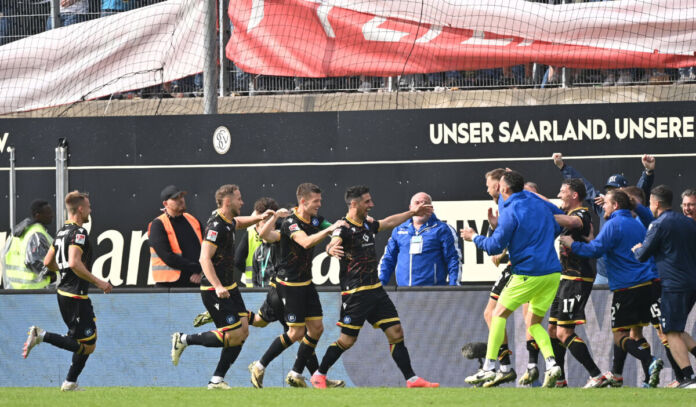 Die Spieler des Karlsruher SC laufen über den Platz bei einem Spiel. Sie freuen sich gerade über ein Tor, deshalb ist der Torjubel der Mannschaft und des gesamten Kaders zu sehen.