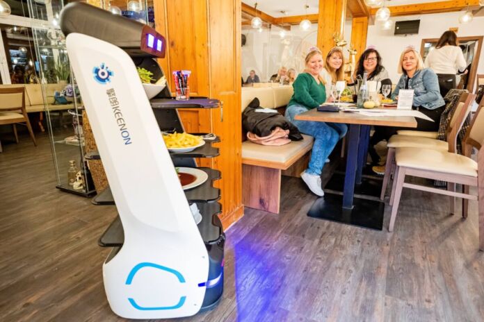 Ein Serviceroboter bringt den Gästen ihre zuvor vollautomatisch bestellten Speisen an den Tisch. Der Roboter fährt sicher durch das Restaurant und wird von den Gästen freudig erwartet.