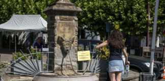 Eine Frau steht vor einem Trinkwasserbrunnen und füllt sich kostenlos ihre Flaschen. Es ist ein heißer, sonniger Tag, das Trinkwasser an diesem Brunnen kostet nichts.