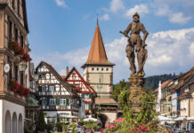 Die steinerne Statue eines Ritters in Rüstung steht in einer charmanten Altstadt vor Fachwerkhäusern und begeisterten Touristen, welche die Gegend erkunden.