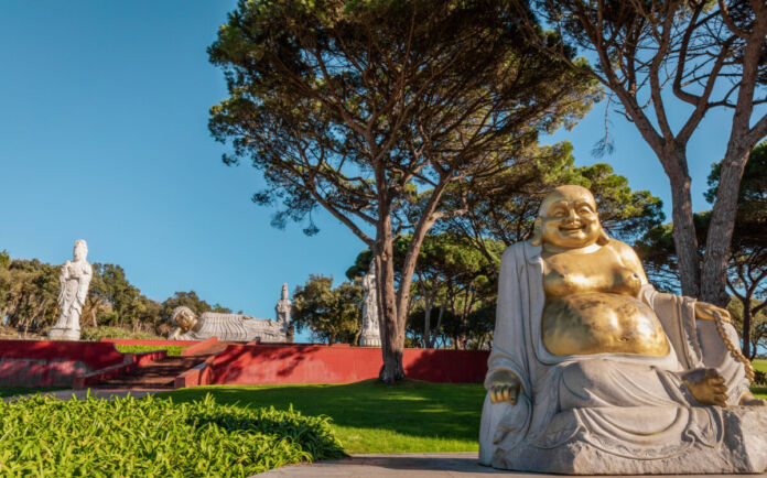 Ein Feng-Shui-Park mit einer goldenen Buddha-Statue im Vordergrund und auf einer Mauer positionierten Statuen anderer buddhistischer Gottheiten lädt den Besucher zum Entspannen und Verweilen ein.