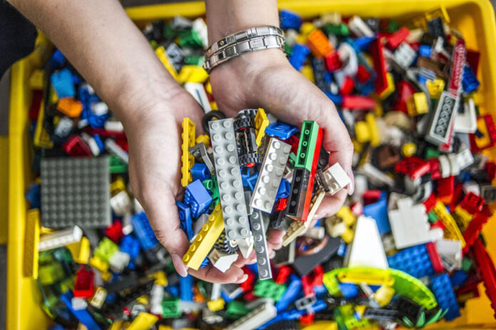 Die Hände eines Mannes greifen in eine volle Kiste mit Legosteinen, beziehungsweise in bunte Bausteine, die mit Steckverbindungen zusammengefügt werden können.
