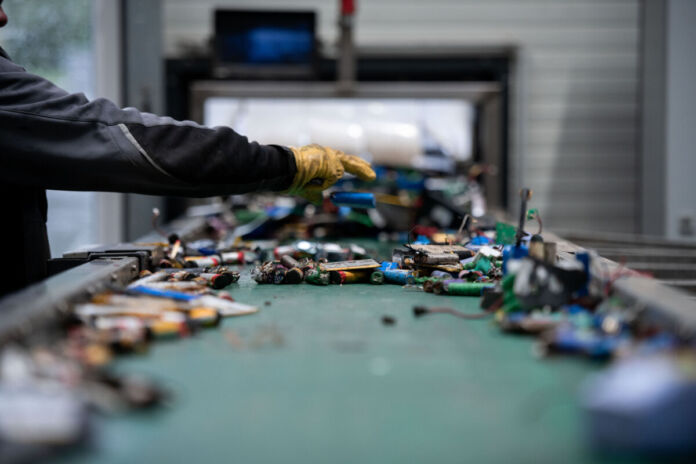 Auf einem Fließband in einer Firma liegen viele Batterien und Akkus von E-Autos. Ein Mitarbeiter ist gerade dabei, diese auszusortieren. Einige Firmen wollen den E-Auto-Akku-Schrott jetzt zum Recyceln verwenden.