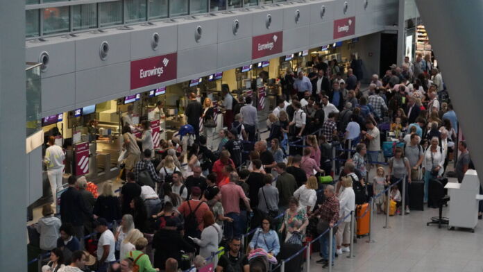 Eine große Menge an Passagieren steht an einem Schalter einer Fluggesellschaft an. Die Menschenmassen haben sich zu einer enormen Schlange angesammelt.