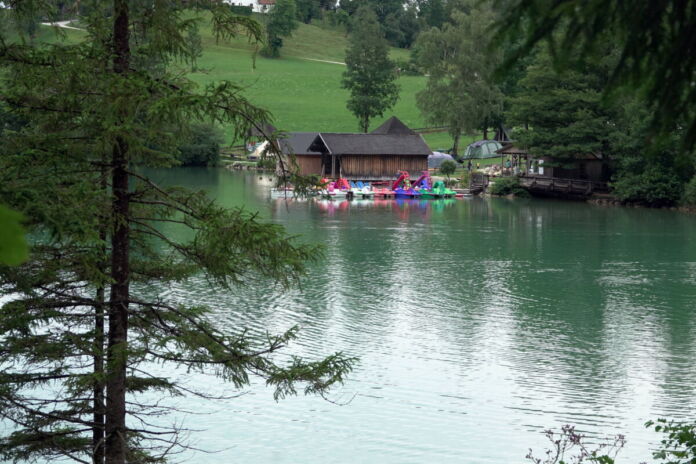 Ein Baggersee oder Badesee - im Hintergrund eine Holzhütte oder ein Ferienhaus mit Bootssteg. Daneben ein Anleger für Urlaubsboote, Kajütboote, Paddelboote und Motorboote.