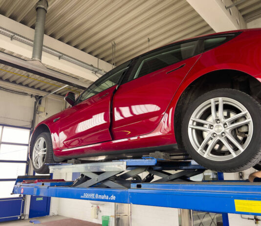 Ein rotes E-Auto der Marke Tesla befindet sich auf der Hebebühne einer Werkstatt. Man führt eine Fahrzeuguntersuchung durch, um mögliche Schäden des Stromers festzustellen. Zehntausende Verbrenner-Autos fallen jetzt durch den TÜV.