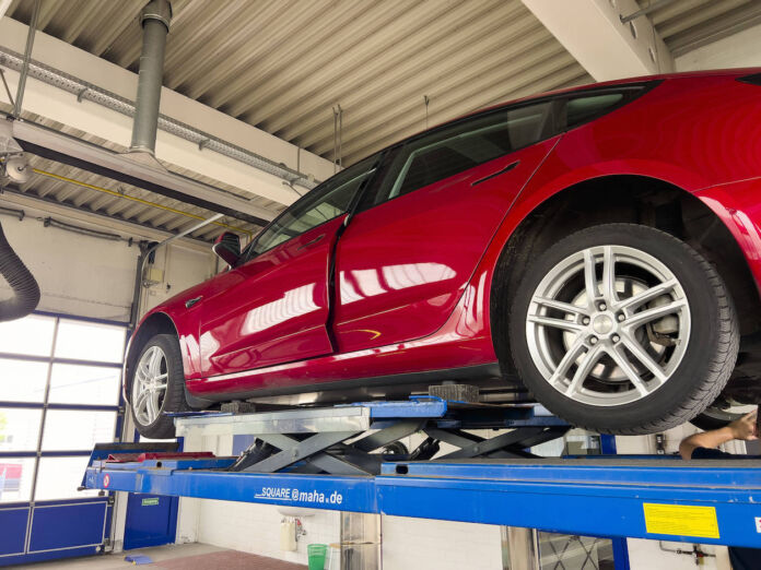 Ein rotes E-Auto der Marke Tesla befindet sich auf der Hebebühne einer Werkstatt. Man führt eine Fahrzeuguntersuchung durch, um mögliche Schäden des Stromers festzustellen. Zehntausende Verbrenner-Autos fallen jetzt durch den TÜV.