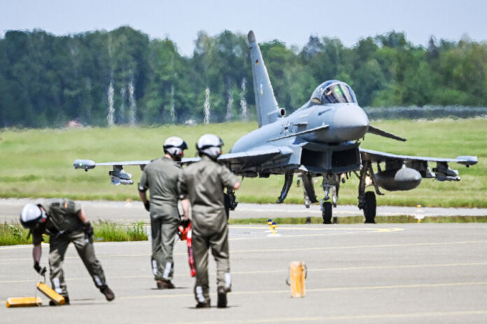 Drei Soldaten der Bundewehr auf einem Landeplatz für Kampfjets. Im Hintergrund steht ein Eurofighter. Die Armee führt auf der abgelegenen Startbahn Übungen durch.