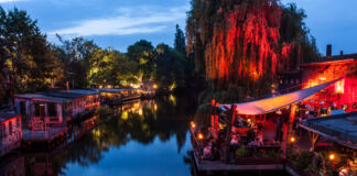 In einer warmen Sommernacht herrscht an beiden Seiten eines Kanals in den zahlreichen Cafés, Kneipen Clubs und Bars reger Betrieb. Menschen feiern auf den Balkonen und Veranden der Etablissments, die mit Lichterketten dekoriert sind.