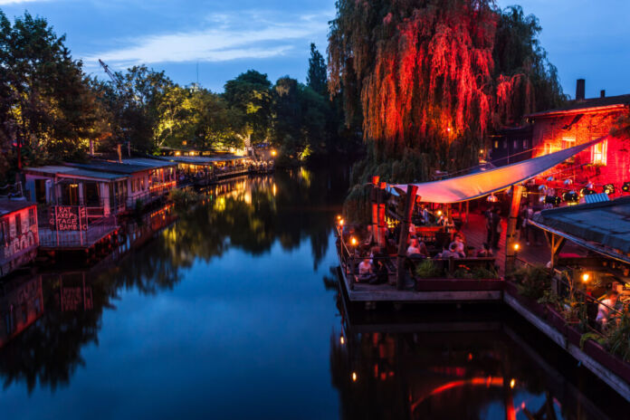 In einer warmen Sommernacht herrscht an beiden Seiten eines Kanals in den zahlreichen Cafés, Kneipen Clubs und Bars reger Betrieb. Menschen feiern auf den Balkonen und Veranden der Etablissments, die mit Lichterketten dekoriert sind.