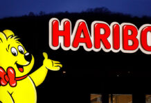 Der berühmte Goldbär von Haribo als Leuchtreklame vor einer Fabrik der Firma Haribo. Es ist noch dunkel und es findet offenbar ein Fabrikverkauf für die Süßigkeiten und das Fruchtgummi des Herstellers statt.