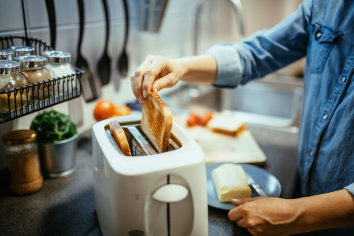 Eine Frau legt eine Scheibe Toastbrot in einen Toaster. Sie möchte das Brot zubereiten, um es später zu essen. Wahrscheinlich wird sie sie mit Käse, Wurst oder Gemüse belegen.