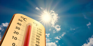 Ein Thermometer in einer Niedrigwinkelansicht. Oben lässt sich ein strahlend blauer Himmel und die Sonne erkennen, die herab scheint. Das Thermometer selbst zeigt fast 50 Grad an. Es ist also sehr warmes Wetter.