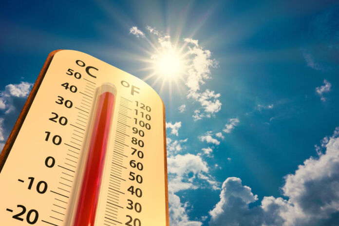 Ein Thermometer in einer Niedrigwinkelansicht. Oben lässt sich ein strahlend blauer Himmel und die Sonne erkennen, die herunterschießt. Das Thermoter selbst zeigt fast 50 Grad an. Es ist also sehr warmes Wetter.
