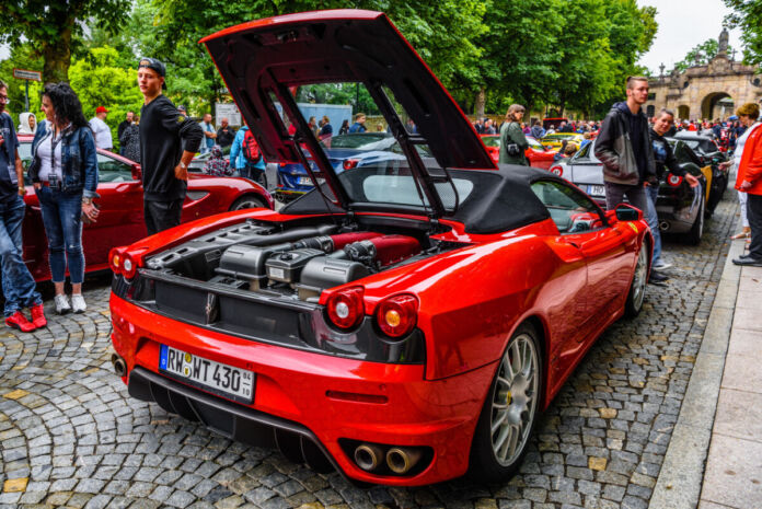 Ein roter Ferrari von hinten. Der Sportwagen steht am Straßenrand. Sein Heck ist geöffnet und offenbart den riesigen V12-Motor. Der Rennwagen ist ein Cabrio.