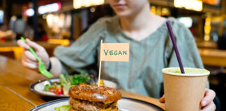 Eine Frau hat in einem veganen Restaurant an einen Burger bestellt. Dazu hat sie ein Getränk und einen kleinen Salat, den sie gerade isst. Eine deutsche Großstadt will jetzt vegan werden.