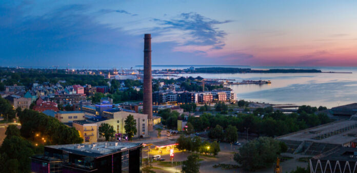 Ein großes Unternehmen oder ein Konzern arbeitet Tag und Nacht. Das Gelände ist hier in der Abenddämmerung dargestellt. Es handelt sich um einen Industriebetrieb mit Hunderten von Beschäftigten. Am Horizont ist das Meer zu sehen.