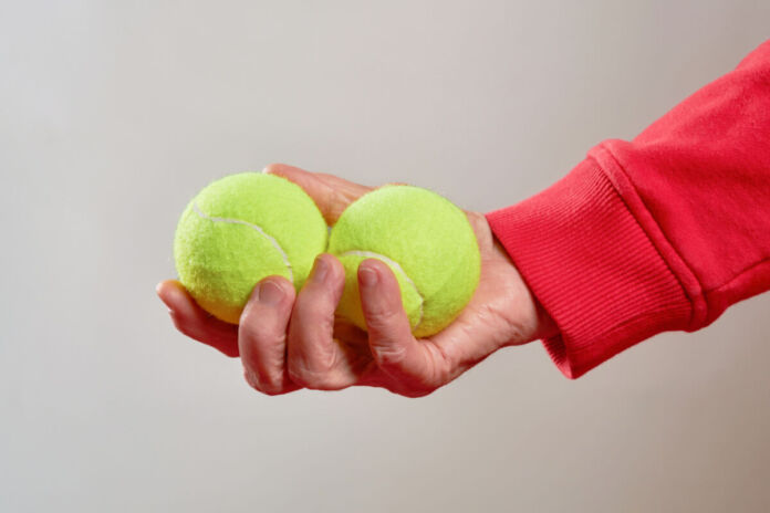 Die Hand eines Mannes hält zwei Tennisbälle in der flachen Hand. Die Bälle sind in einem leuchtenden Limettengrün. Der Mam hält die Tennisbälle in die Kamera.