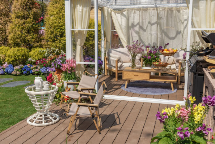 Auf einer Terrasse, die in einen gepflegten Garten führt, befindet sich ein Pavillion, unter dem sich ein kleiner Tisch und gemütliche gepolsterte Liegen befinden.