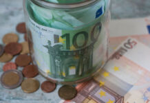 In einem Glas befinden sich mehrere Geldscheine, daneben liegt Kleingeld in Münzen. Es sind 100 Euro Scheine und 50 Euro Scheine dabei.